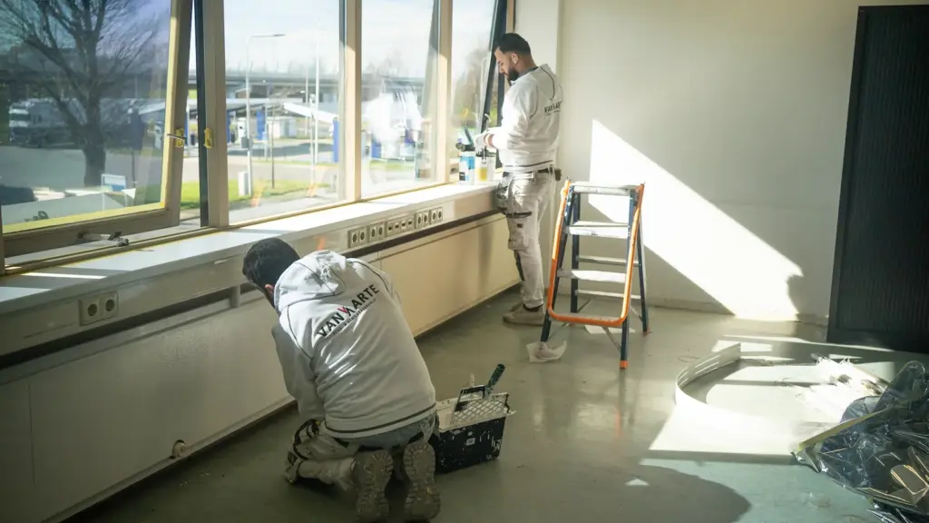 Schilders van Van Arte aan het werk bij een groot raam